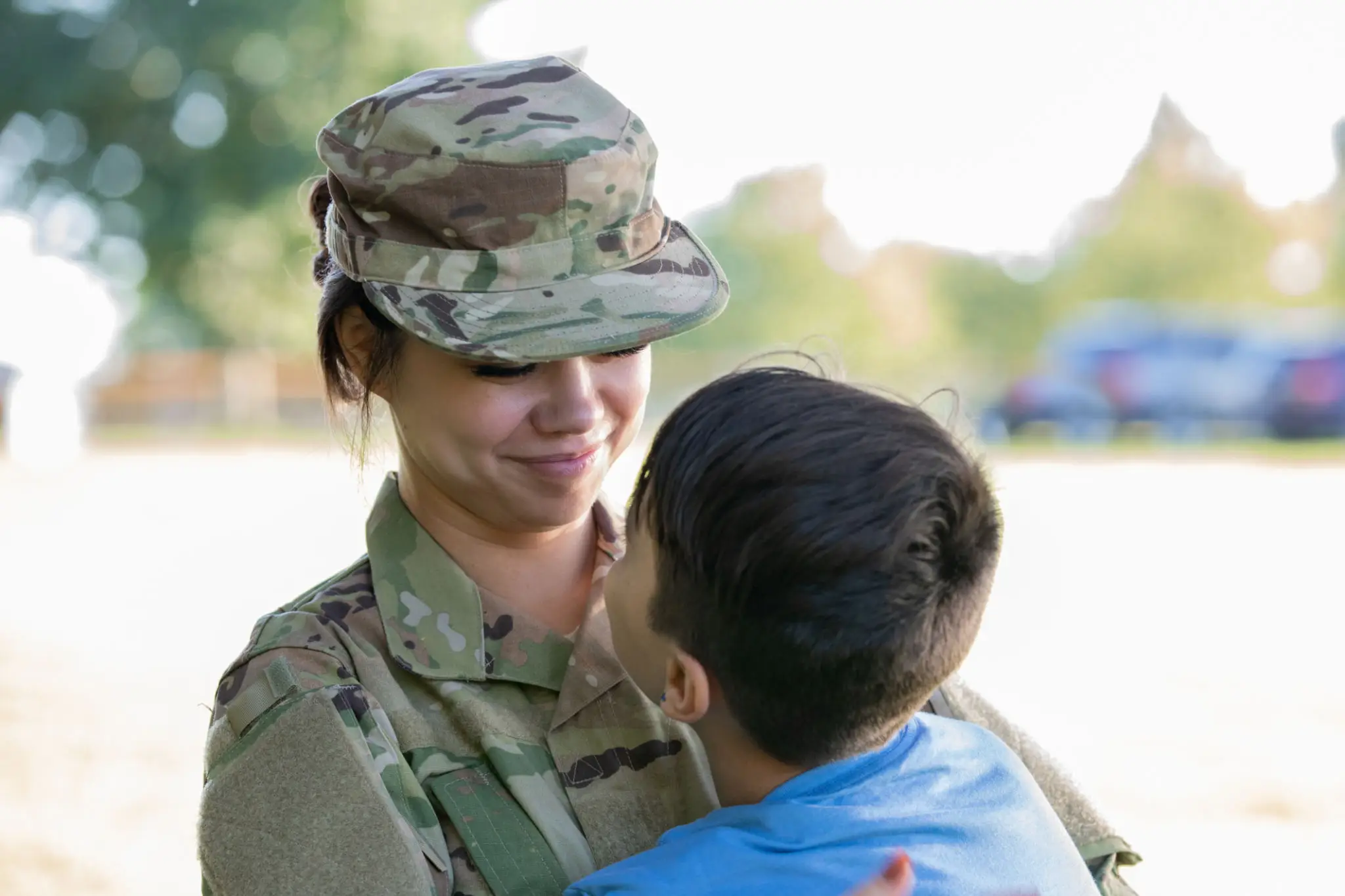 A soldier smiling warmly at a child in her arms outdoors.