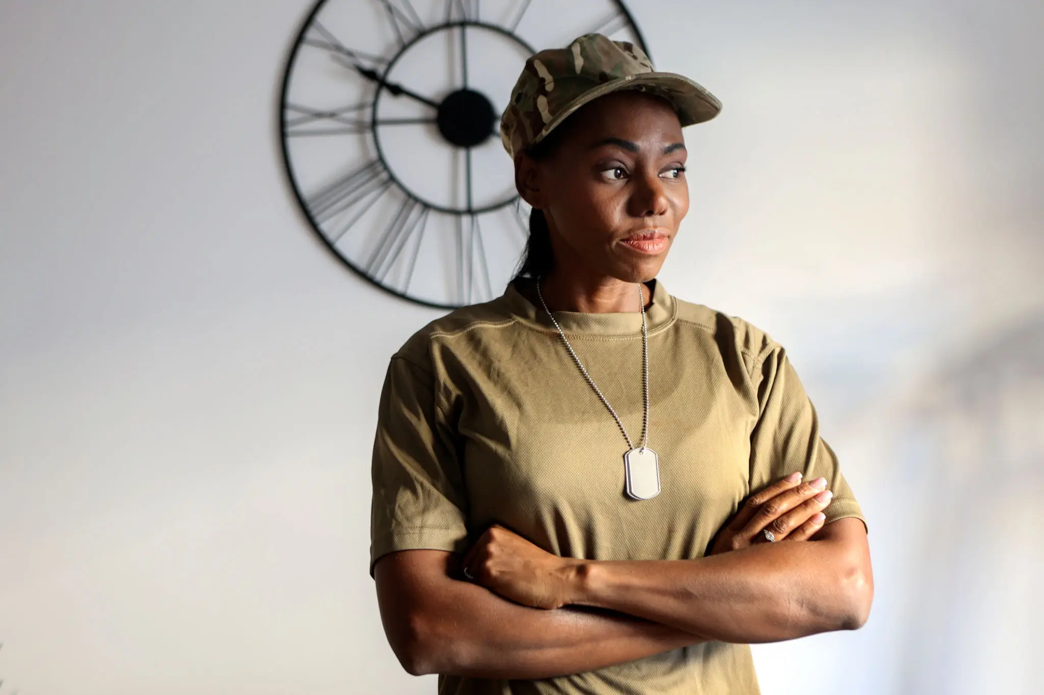 Young woman in a cap and dog tags standing confidently with arms crossed.