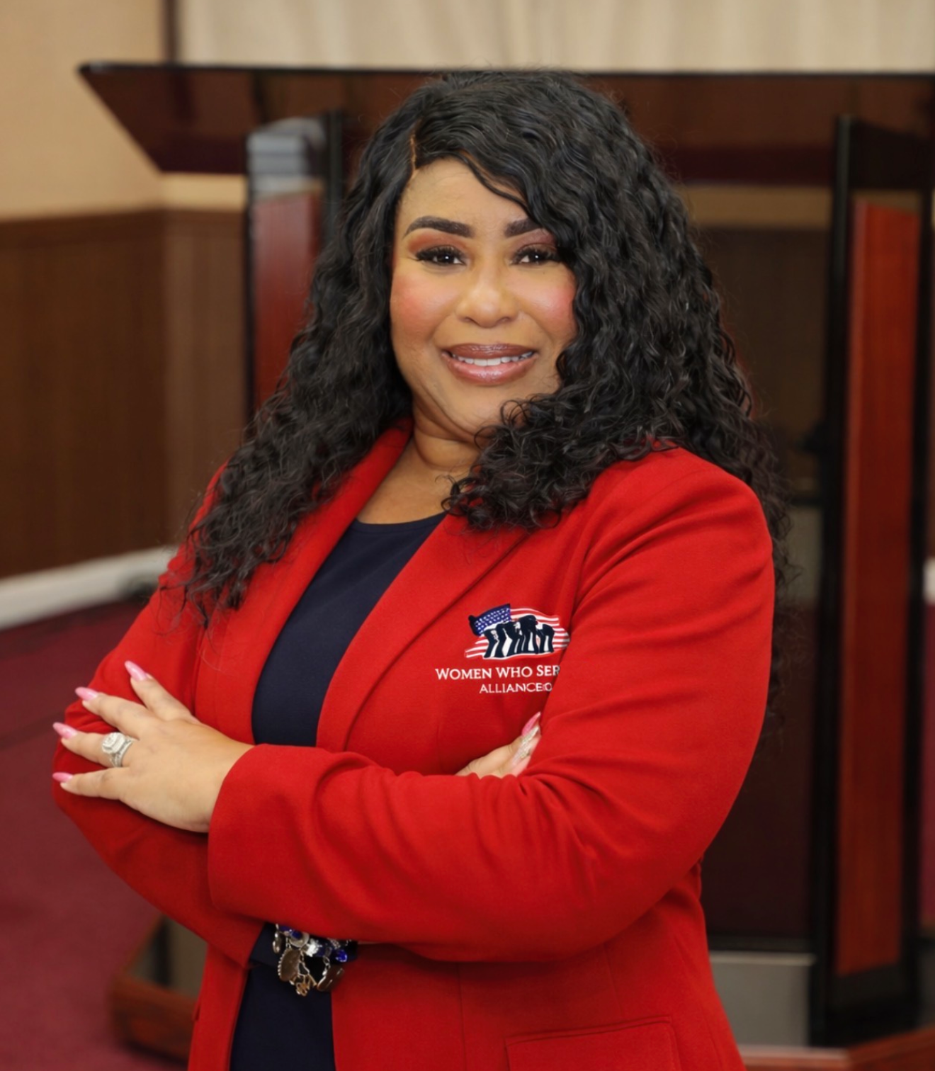 Woman in red blazer smiling confidently indoors.