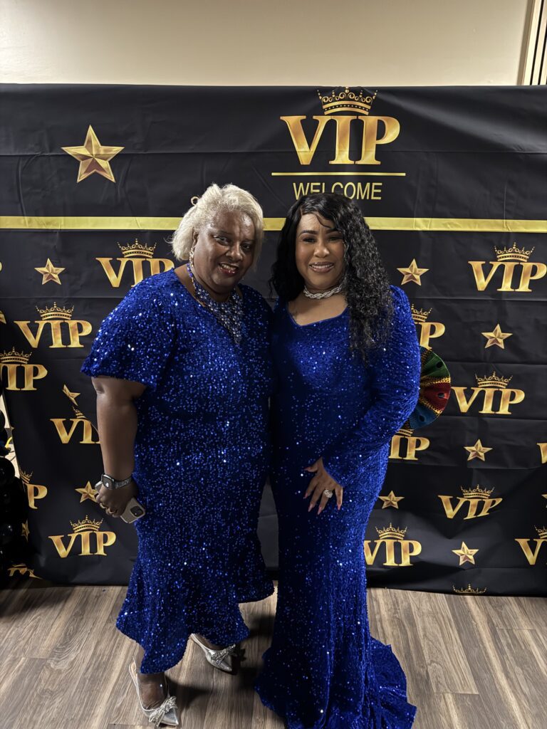 Two women in matching blue dresses pose at a VIP-themed event.