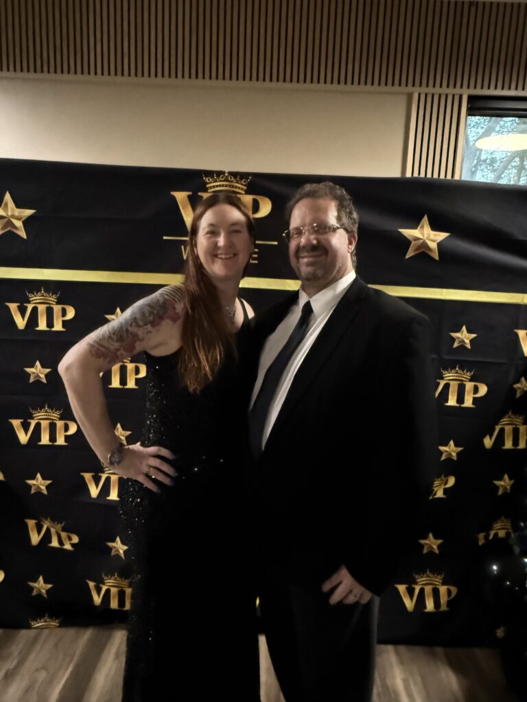 A couple dressed formally at a VIP event with a star-themed backdrop.