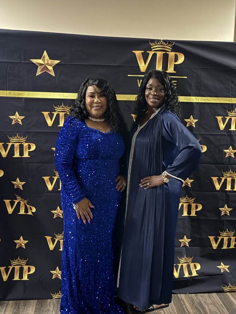 Two women dressed elegantly posing in front of a VIP backdrop.