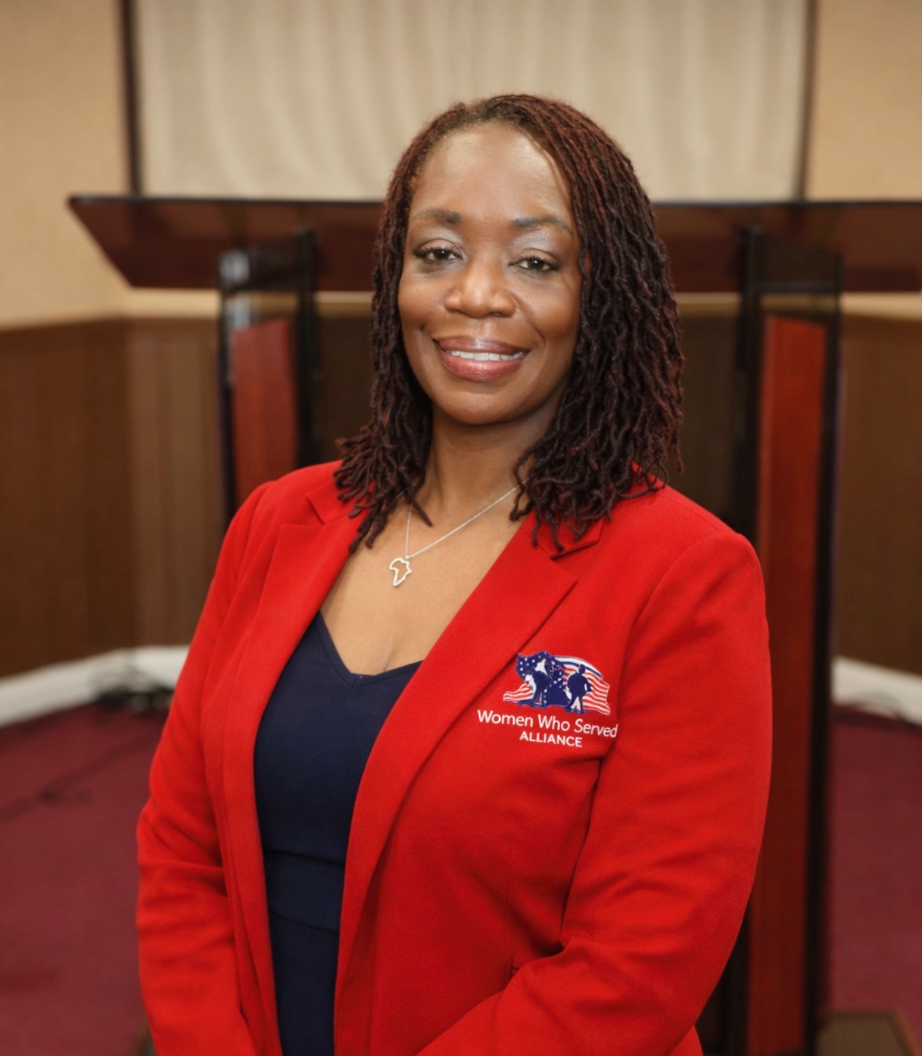 A smiling woman wearing a red blazer indoors.