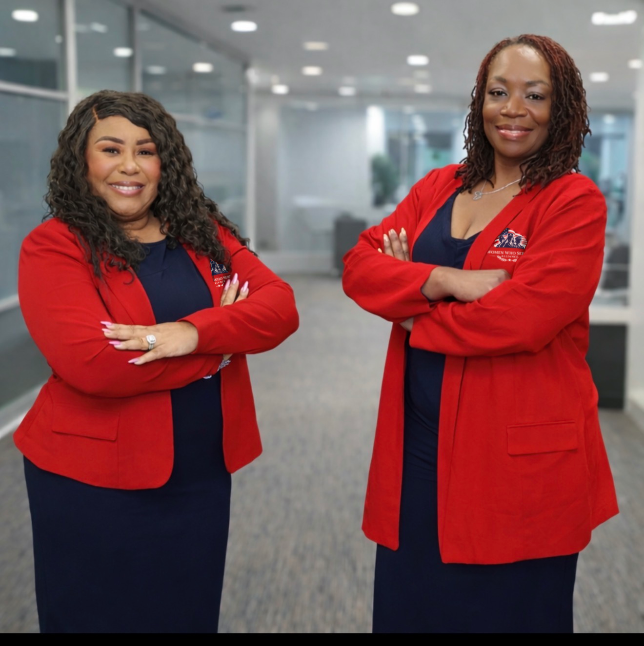 Two professional women in red blazers smiling confidently in an office.