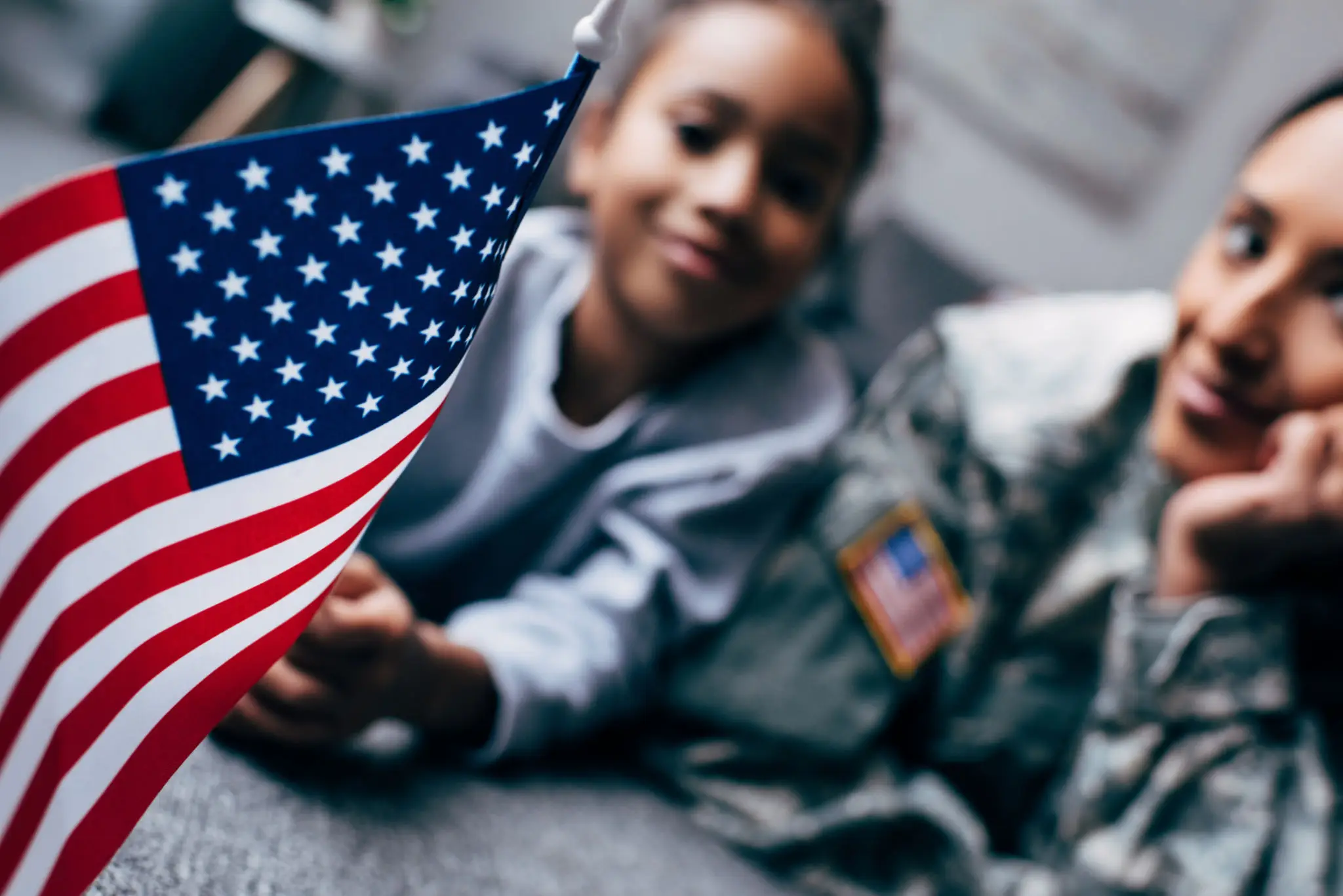 A child holds an American flag near a person in military uniform.